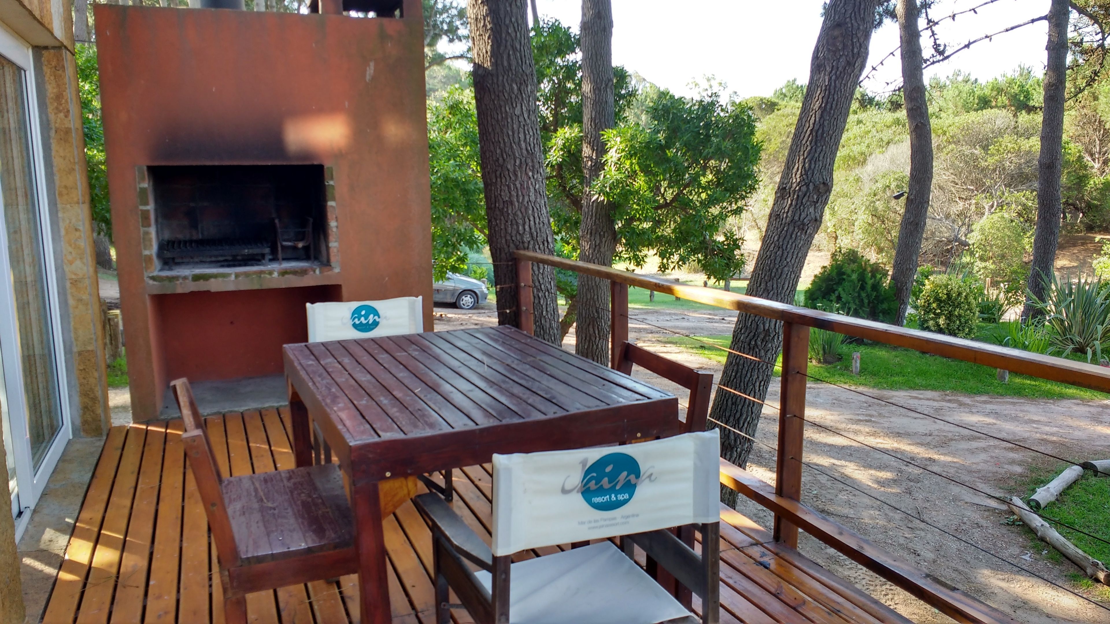 Eine Terrasse im Freien mit Holztisch und -stühlen, einem Grill und einem Geländer.