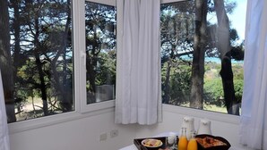 A room with a large window overlooking a forest. There is a tray with breakfast items and two bottles of orange juice on the windowsill. - Jaina Resort & Spa (Mar de Las Pampas)