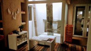 A room with a wooden floor, a white desk with a plant, a dreamcatcher, and a window with a view of a tree. - Jaina Resort & Spa (Mar de Las Pampas)