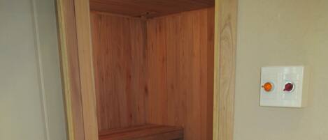 Una sauna de madera con un banco, un lavabo blanco con lavamanos de azulejos y un interruptor de luz en la pared.