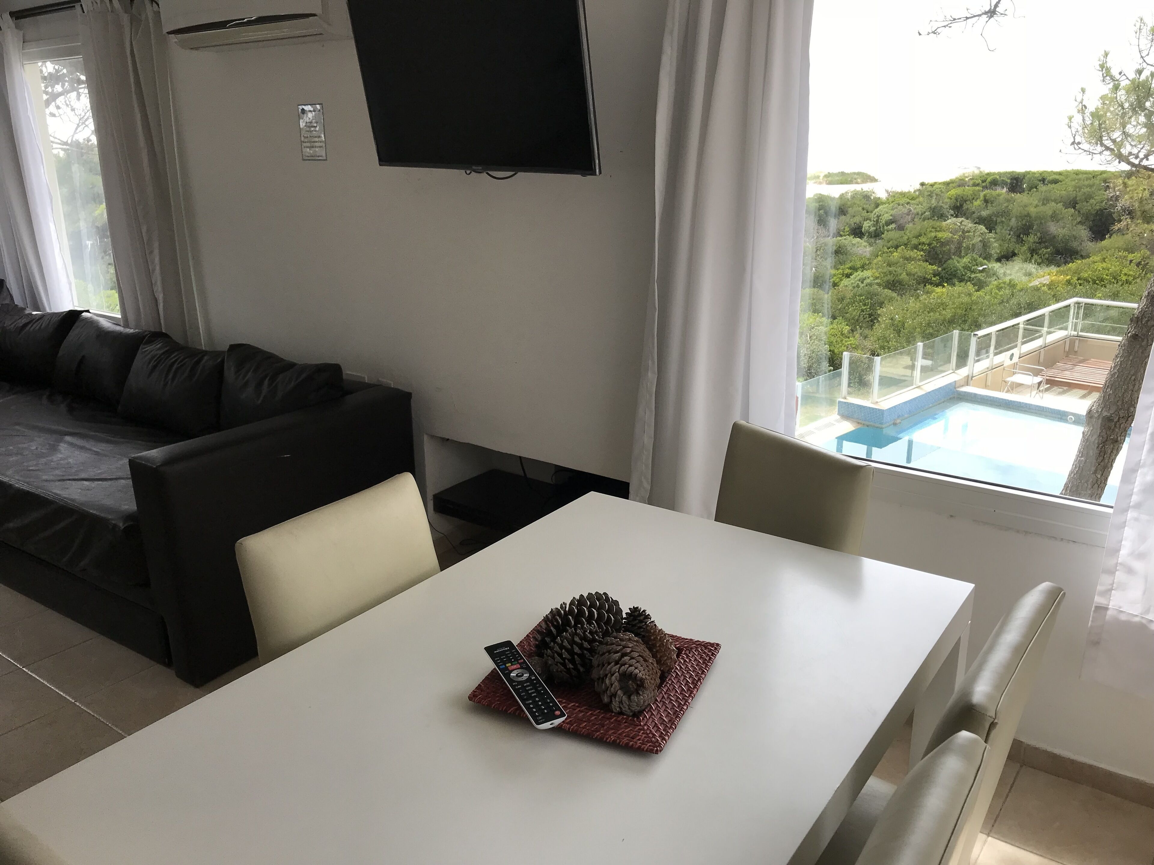 A modern living room with a white table, a black sofa, and a TV mounted on the wall.