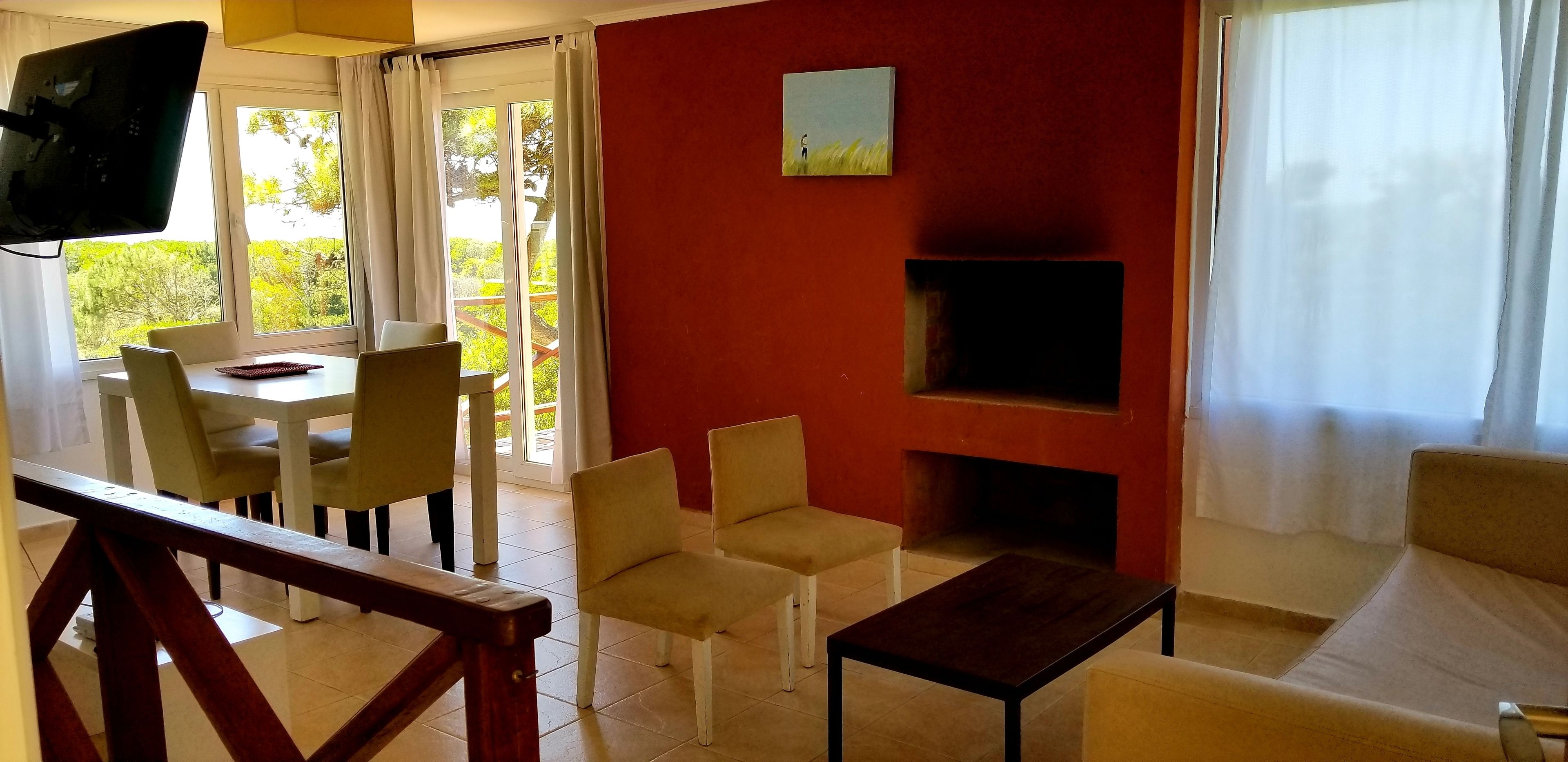 Un salon avec un mur rouge, une cheminée, un téléviseur et un coin repas comprenant des chaises et une table.