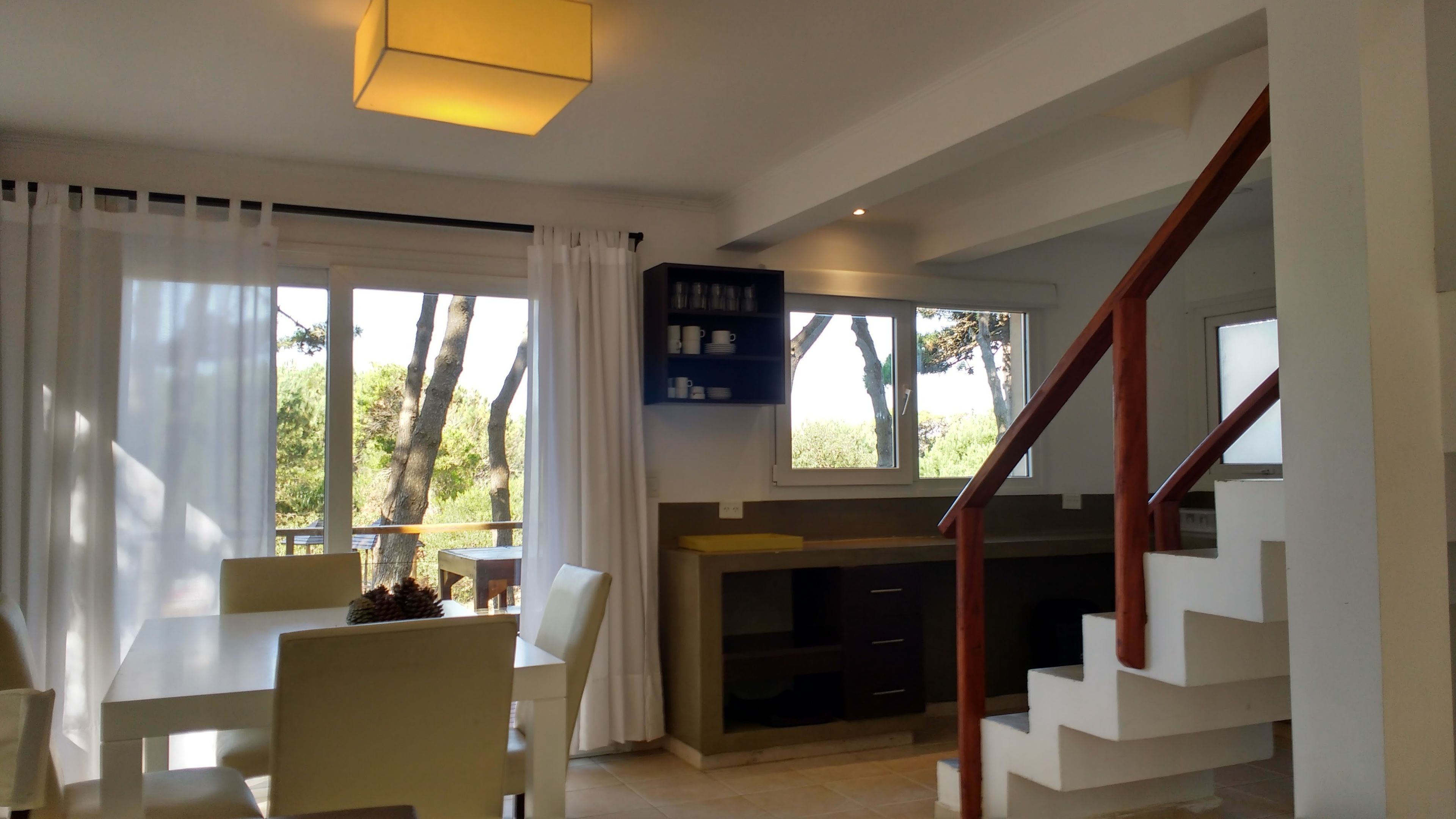 A modern living room with a dining area, large windows, and a staircase.