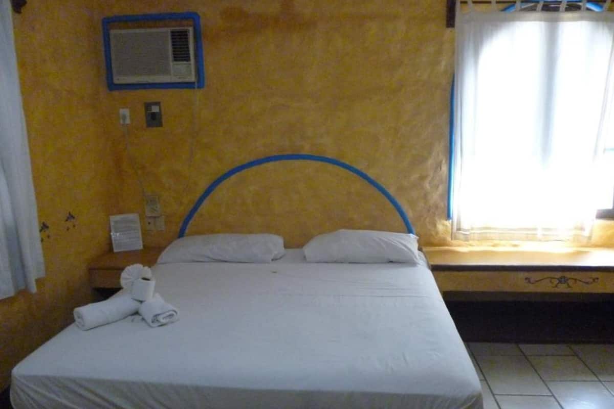 A single bed with a blue headboard, white bedding, and a rolled towel on the footboard.