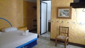 Habitación de hotel con una cama, una silla, una puerta y un cuadro colgado en la pared.