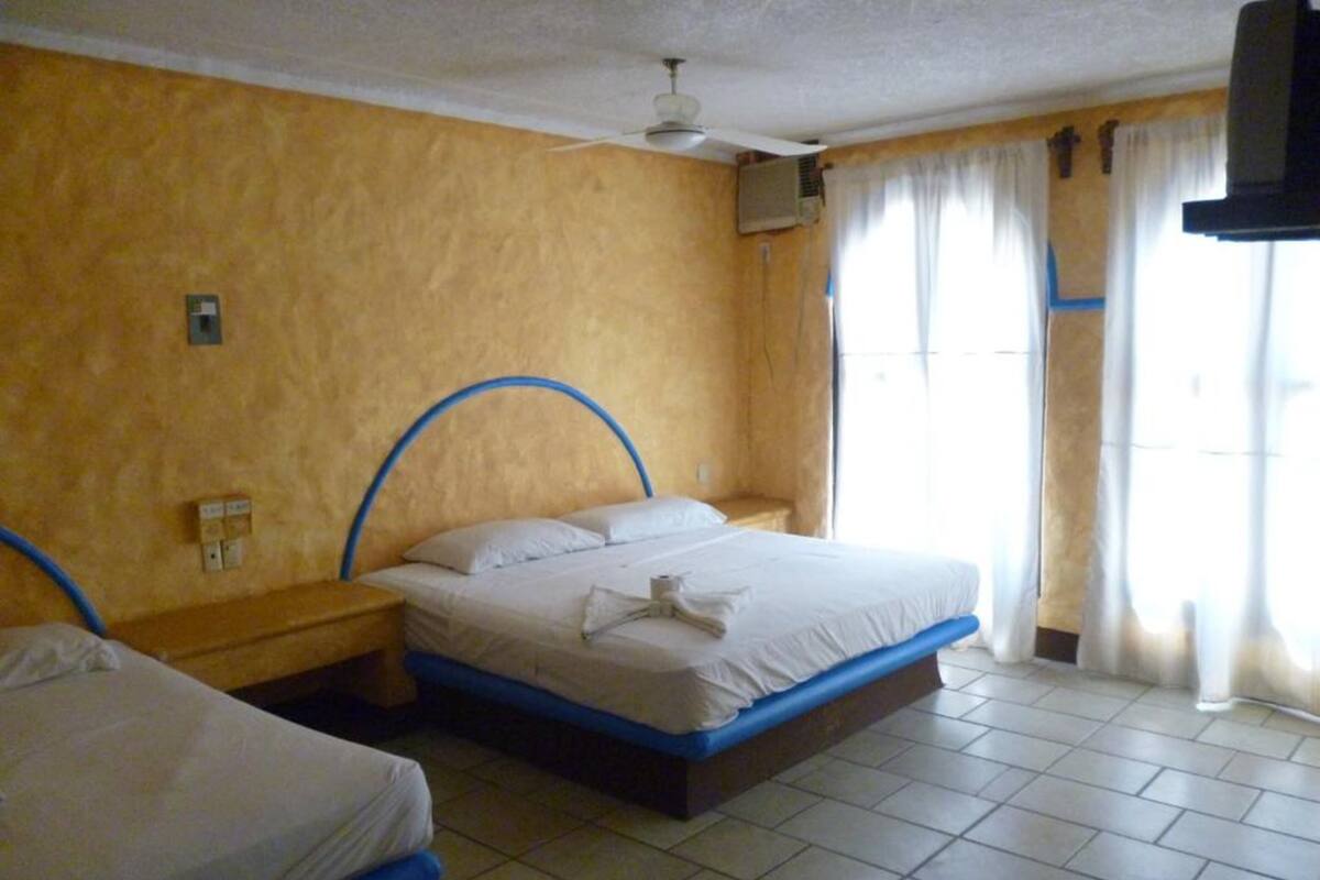 A hotel room with two beds, a ceiling fan, an air conditioning unit, and a window with curtains.