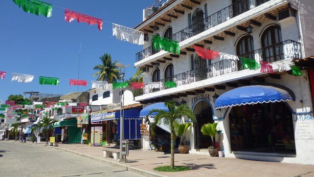 Una calle bordeada de edificios, algunos con balcones y toldos, bajo cielos despejados.