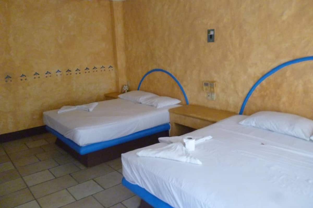 A hotel room with two beds, each with a blue headboard, white bedding, and a towel on the bed.