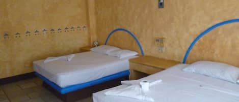 Habitación de hotel con dos camas, cada una con cabecera azul, ropa de cama blanca y una toalla sobre la cama.