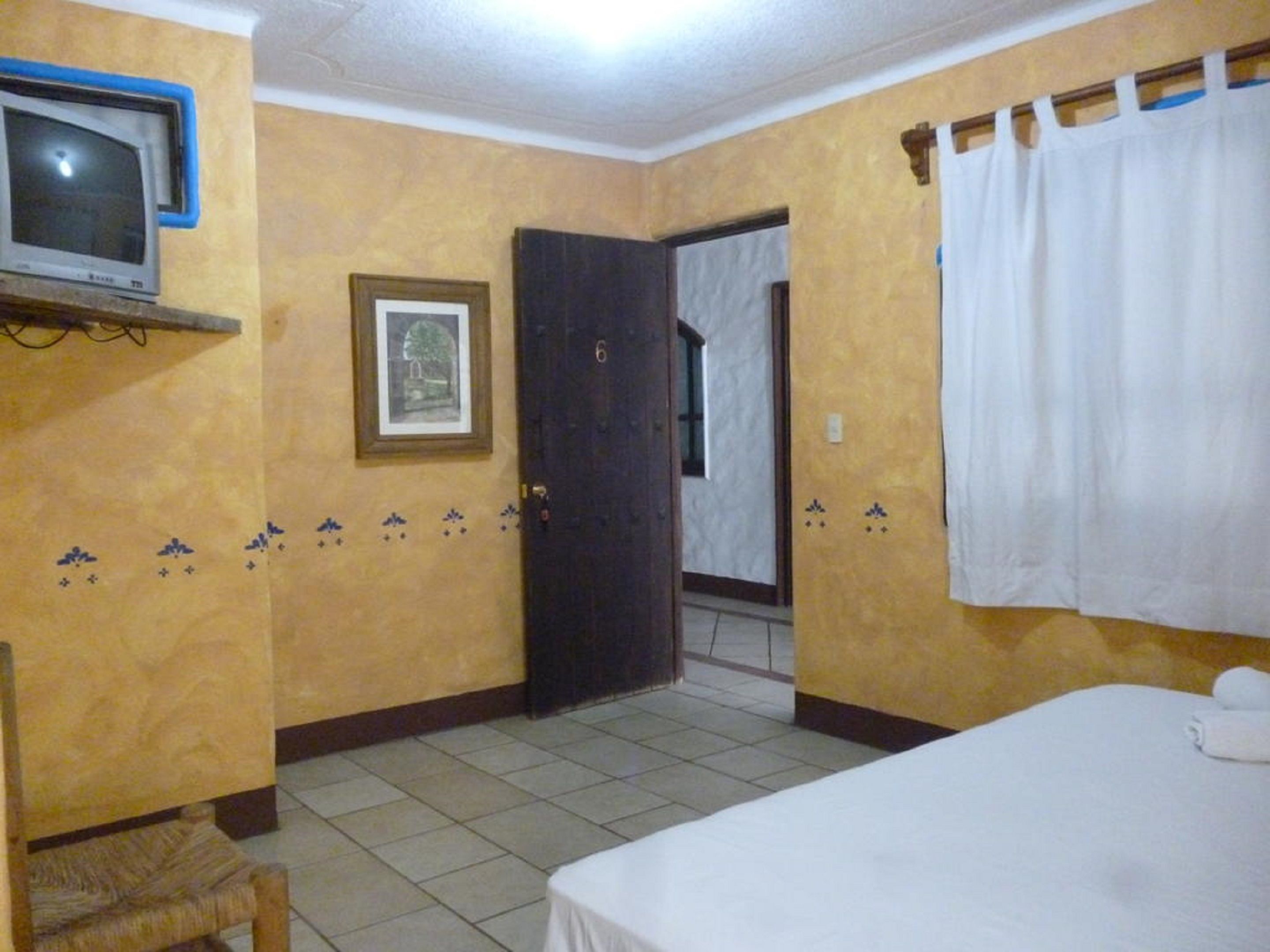 A hotel room with a bed, a television, a door, and a window with curtains.