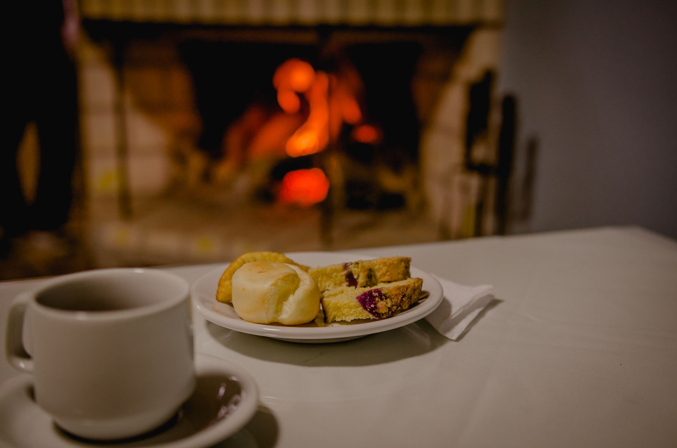 A table with a white cup and a plate of food, a fireplace in the background.