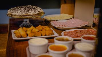 Uma mesa com diversos alimentos, incluindo torta, queijo, presunto e molhos para acompanhar.