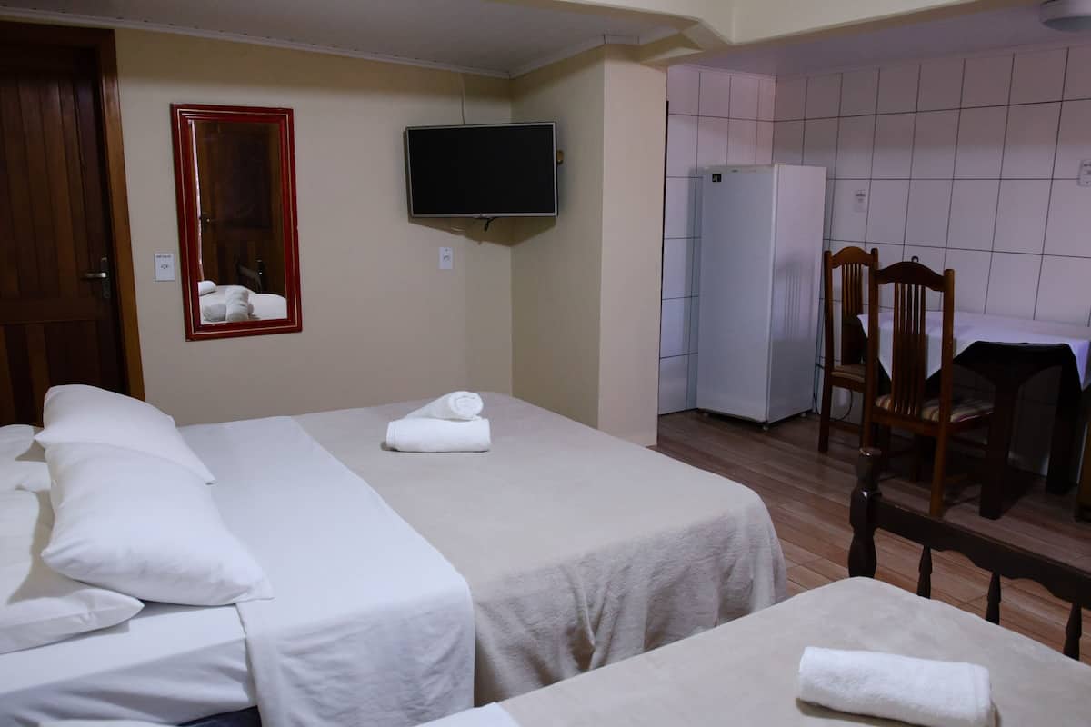 Quarto de hotel com duas camas, televisão, espelho, frigorífico e área de refeições com cadeiras.