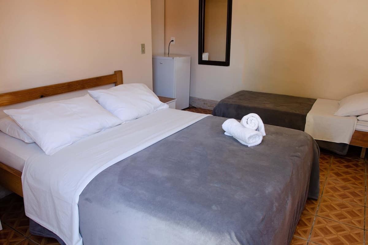 Quarto de hotel com uma cama grande, uma cama menor, uma escrivaninha e um frigorífico.