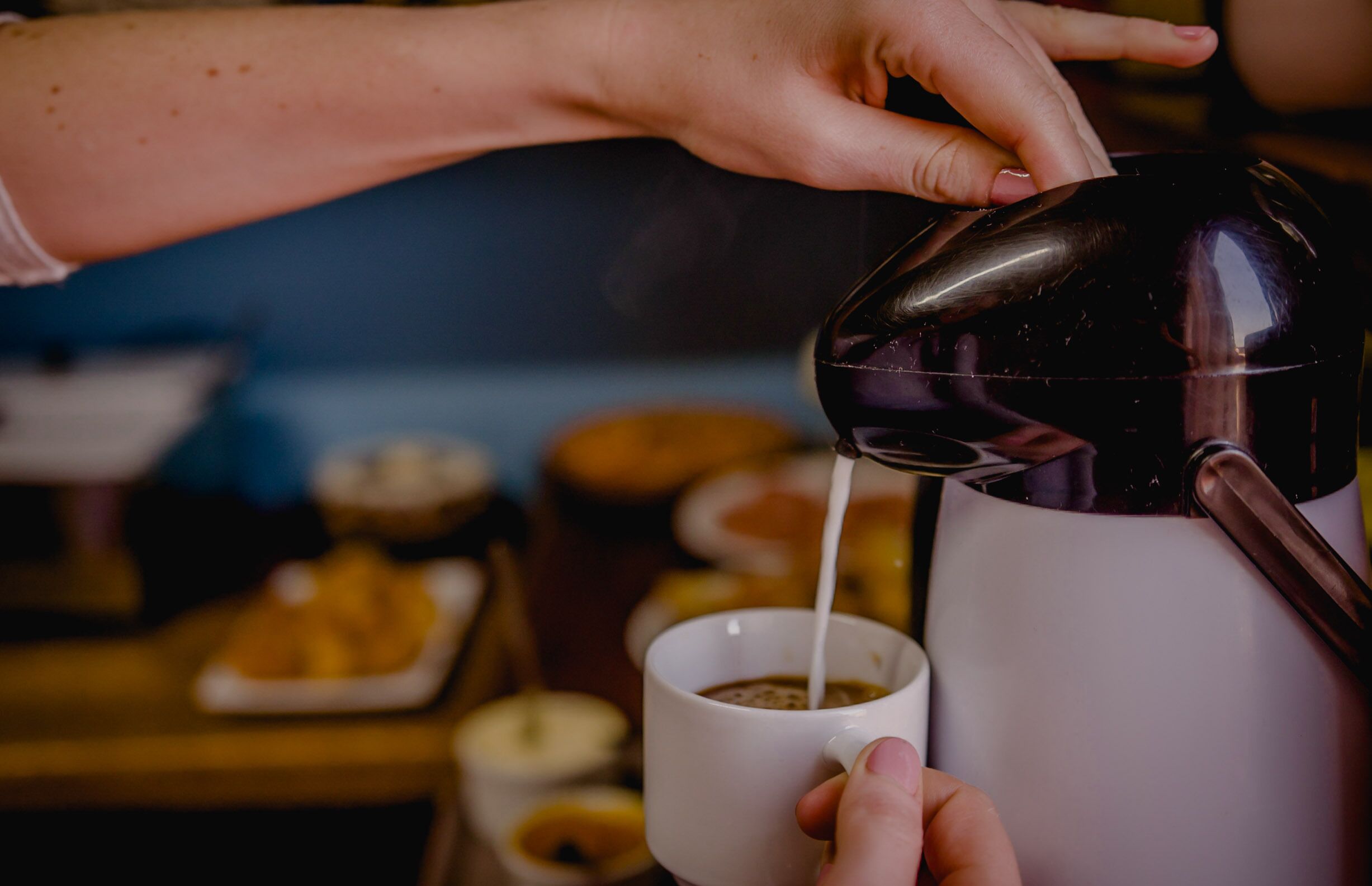 A hand pouring milk into a cup of coffee.