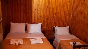 A room with two beds, wooden walls, and a nightstand with a lamp.
