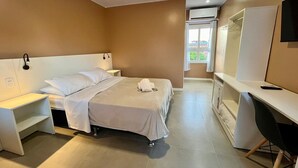 Une chambre d’hôtel comprenant un lit, des tables de chevet, un bureau, une chaise, un téléviseur et un appareil de climatisation.