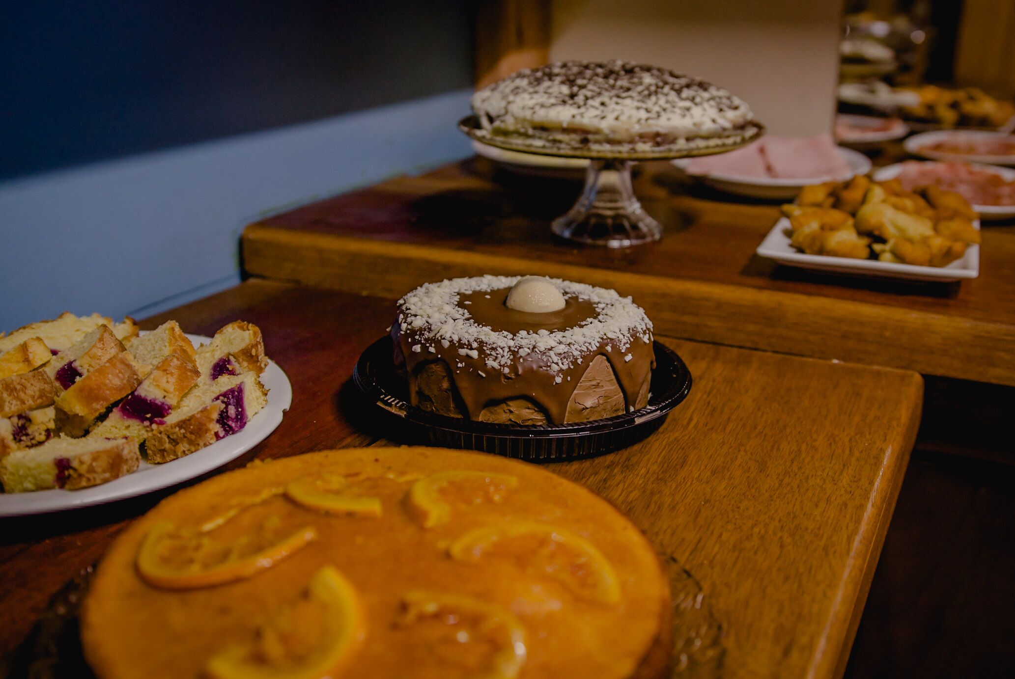 Variedad de postres sobre una mesa de madera, incluyendo un pastel con cobertura blanca, una tarta con rodajas de naranja y un pastel con glaseado de chocolate.