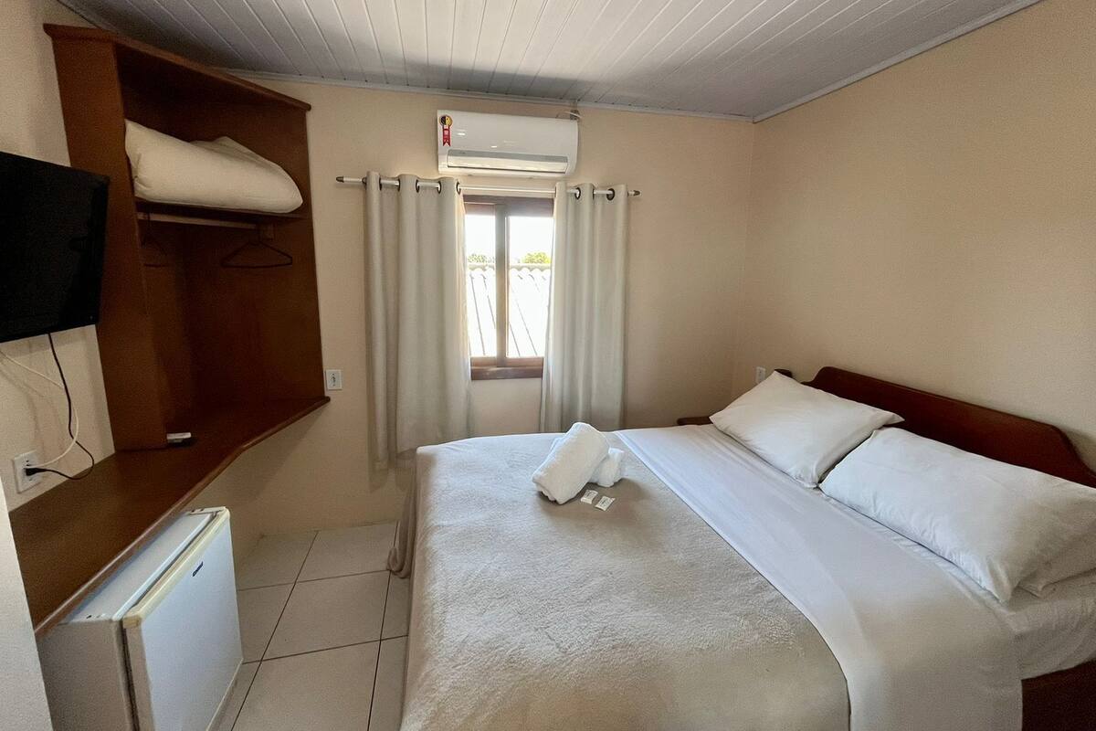 Quarto de hotel com cama, televisão, ar condicionado e janela com cortinas.