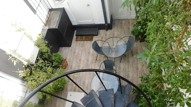Eine Wendeltreppe führt zu einer Terrasse mit Gartenmöbeln und Topfpflanzen.