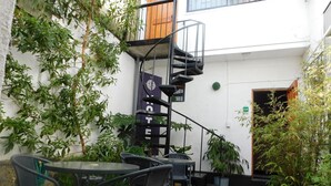 Ein Innenhof mit Sitzgelegenheiten im Freien, einer Wendeltreppe und zahlreichen Blumentöpfen.