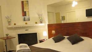 Ein Hotelzimmer mit einem großen Bett, einem Kamin, einem Flachbildfernseher und einem Spiegel an der Wand.