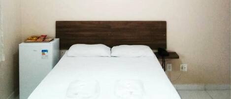 Habitación de hotel con cama, mesita de noche, refrigerador pequeño y un cuadro en la pared.
