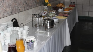 A buffet table with various food items, a water dispenser, and a vase with flowers. - Bica Pau Hotel Thermas (Caldas Novas)