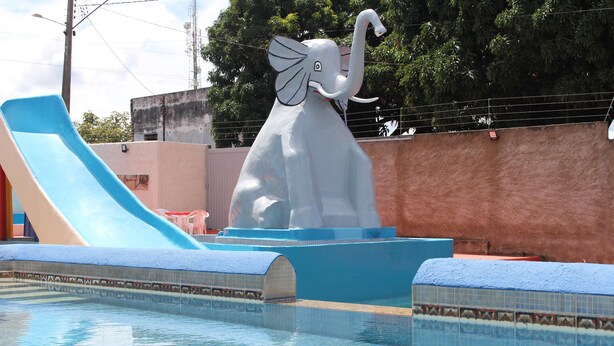 A swimming pool with a large elephant sculpture, a blue slide, and a tiled deck. - Bica Pau Hotel Thermas (Caldas Novas)