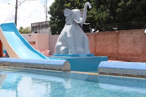 Ein Schwimmbecken mit einer großen Elefantenskulptur, einer blauen Rutsche und einer gefliesten Liegefläche.