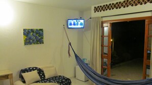 A living room with a sofa, a hammock, a TV, and a door leading outside. - Casa Tara (Santa Marta)