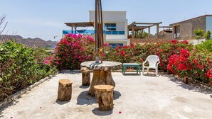 A modern building with a balcony, surrounded by vibrant bougainvillea bushes and a concrete patio with wooden stools and a white plastic chair. - Casa Tara (Santa Marta)