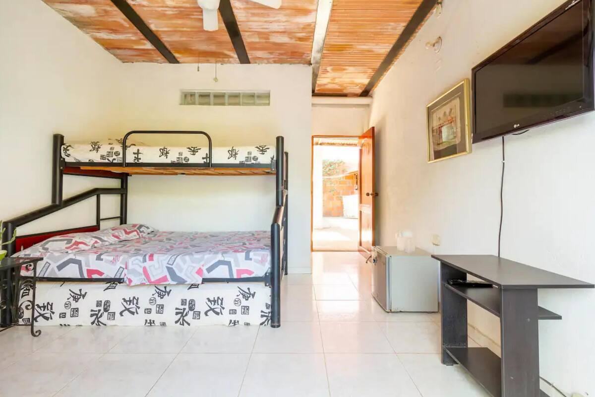 A room with a bunk bed, a desk, a television, and a ceiling fan.