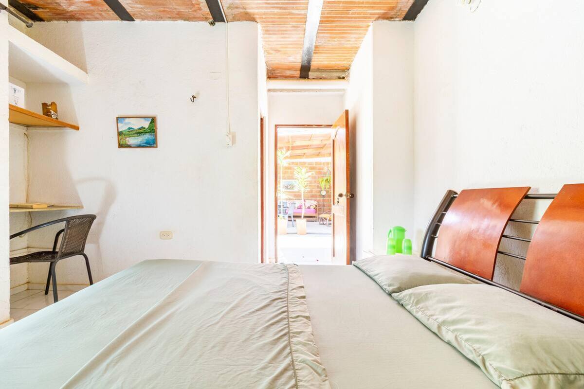 A bedroom with a bed, a desk, and a chair. There is a door leading to an outdoor area.