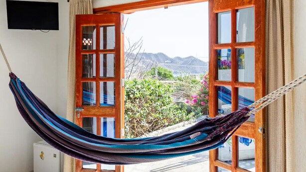 A hammock hanging between open wooden doors with a view of mountains and greenery outside. - Casa Tara (Santa Marta)