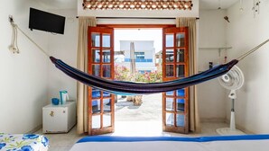 A room with a hammock, a bed, a TV, a fan, and a view of the outside. - Casa Tara (Santa Marta)