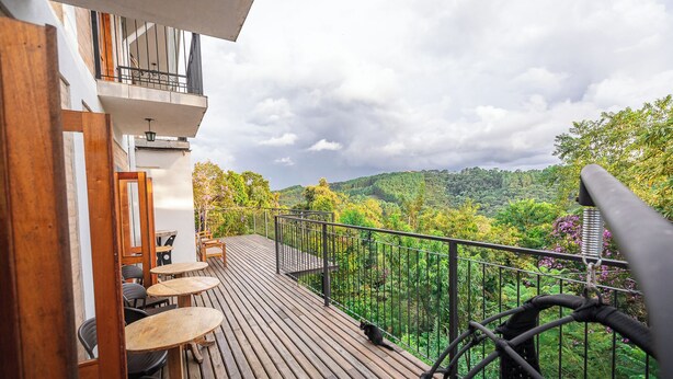 A wooden deck with outdoor seating, a balcony with a metal railing, and a view of a forested hillside. - Villa Hegus (Campos do Jordão)