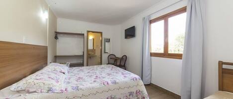 Un dormitorio con cama, televisión, ventana con cortinas y cabecero de madera.