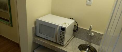 A compact kitchenette with a white microwave, a sink, and a small refrigerator.
