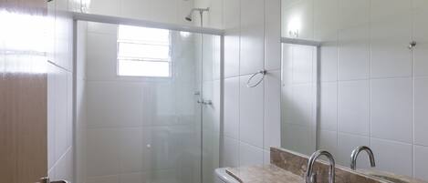 A modern bathroom with a glass-enclosed shower, a sink with a marble countertop, and a large mirror.