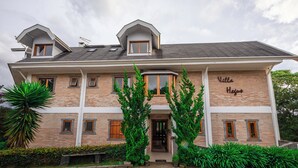 A two-story building with a brick facade, a balcony, and a sign that reads "Villa Hejnu". - Villa Hegus (Campos do Jordão)