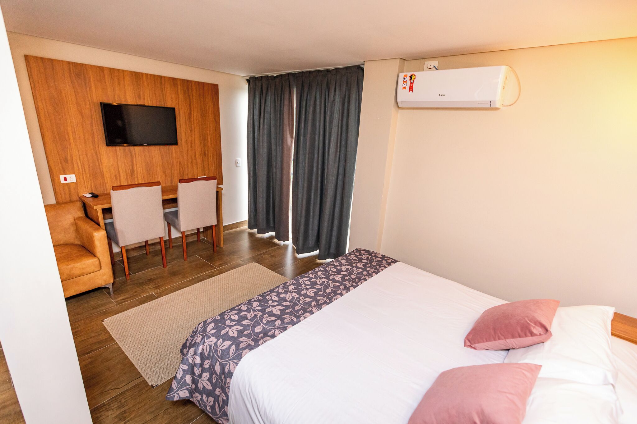 Habitación de hotel con cama, escritorio, sillas, televisor y aire acondicionado.