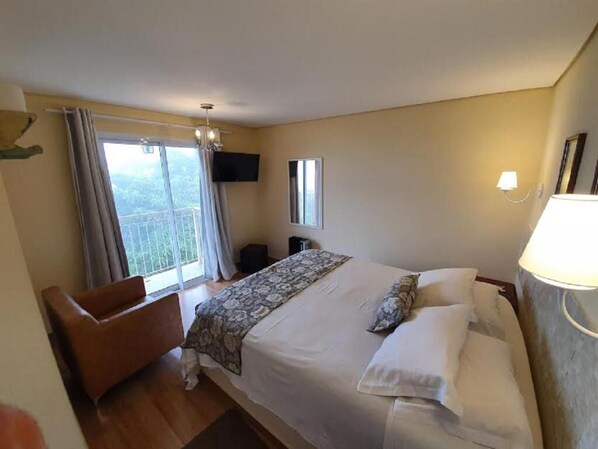 Habitación de hotel con una cama grande, una silla, un televisor, una ventana con cortinas y una lámpara.