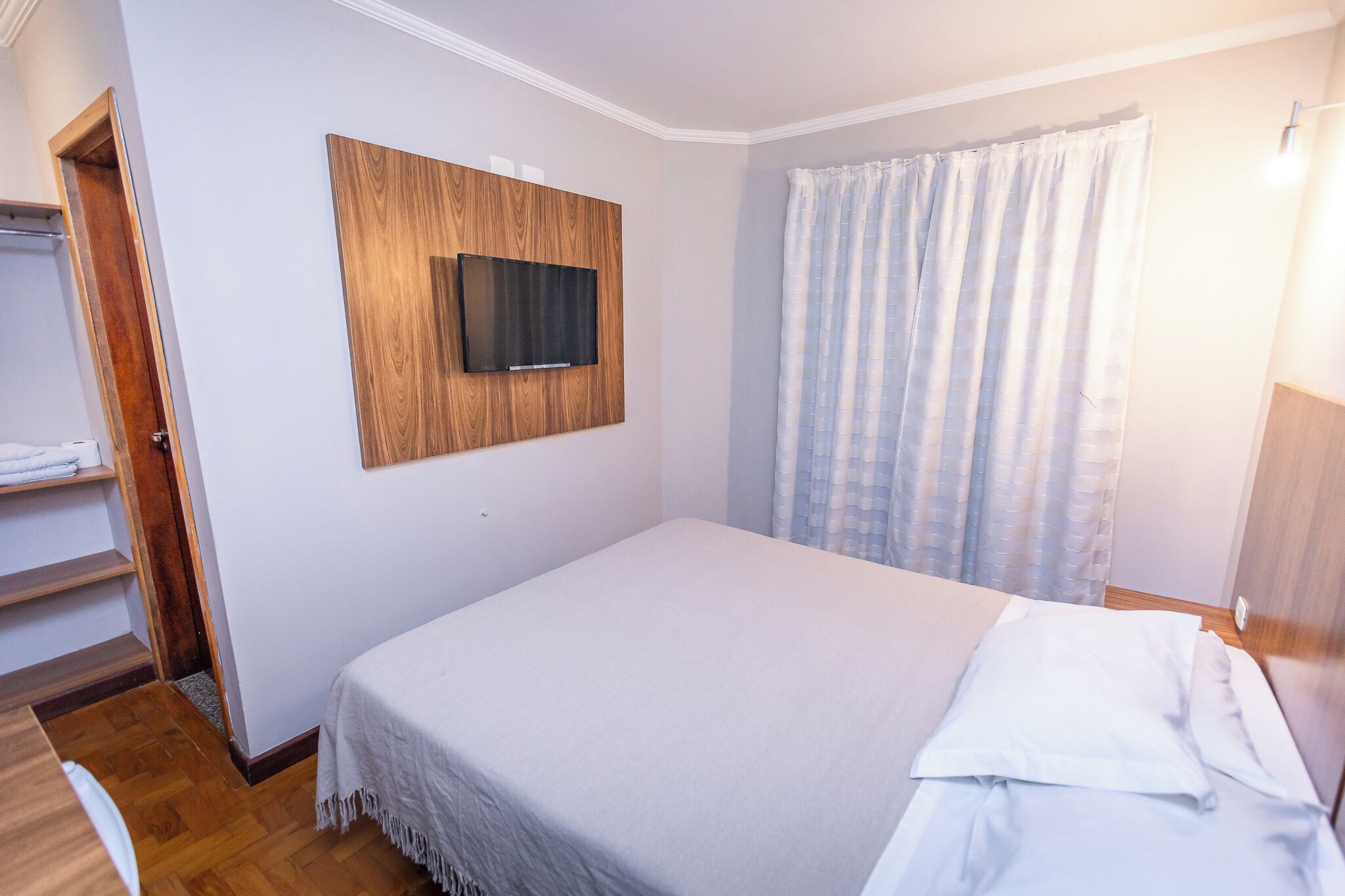 Een slaapkamer met een bed, een aan een houten paneel bevestigde televisie, een douchegordijn en een houten deur.