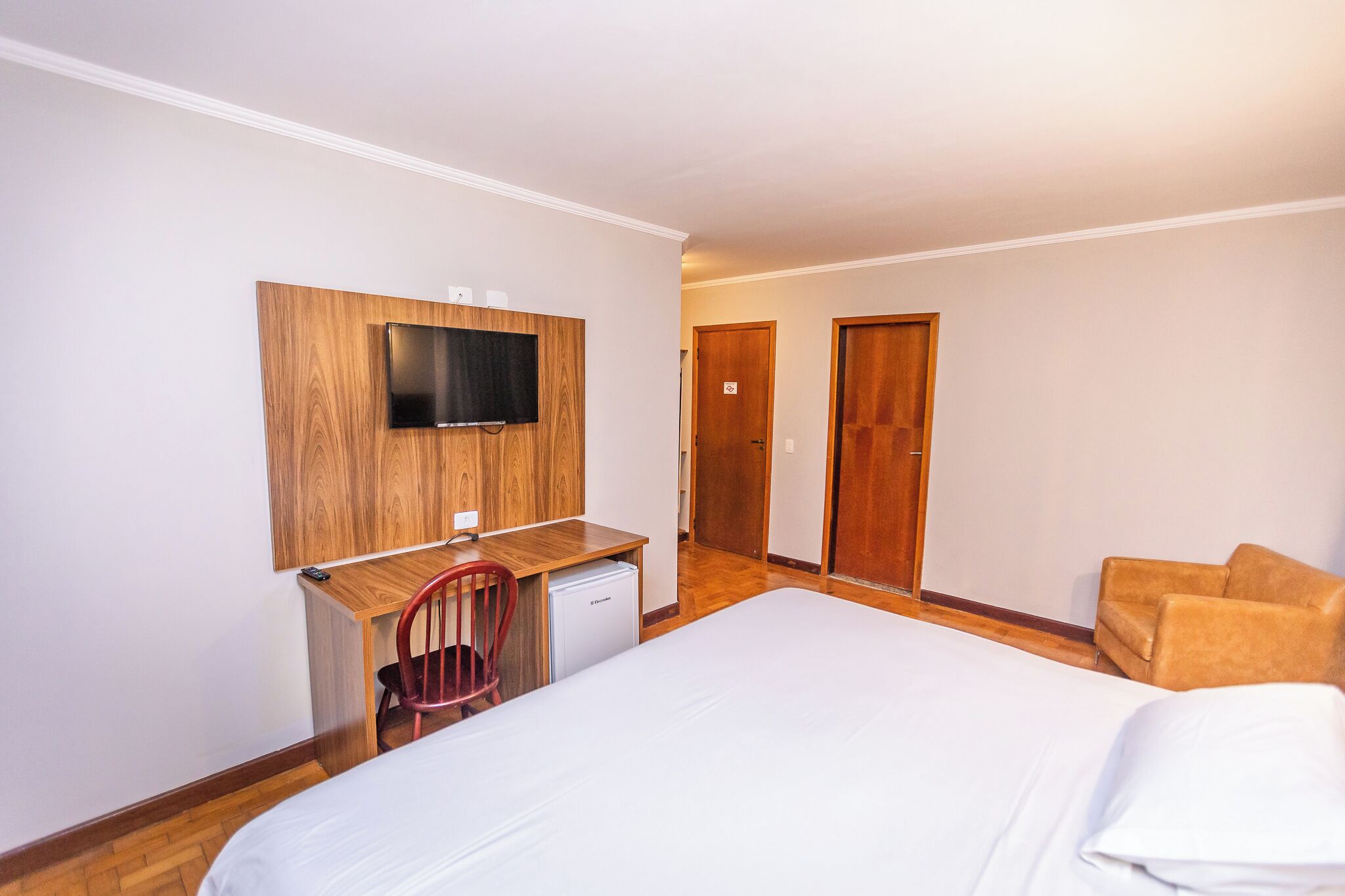 Une chambre d’hôtel comprenant un lit, un bureau avec une télévision, une chaise et une armoire.