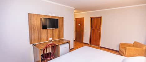 A hotel room with a bed, a desk with a television, a chair, and a wardrobe.
