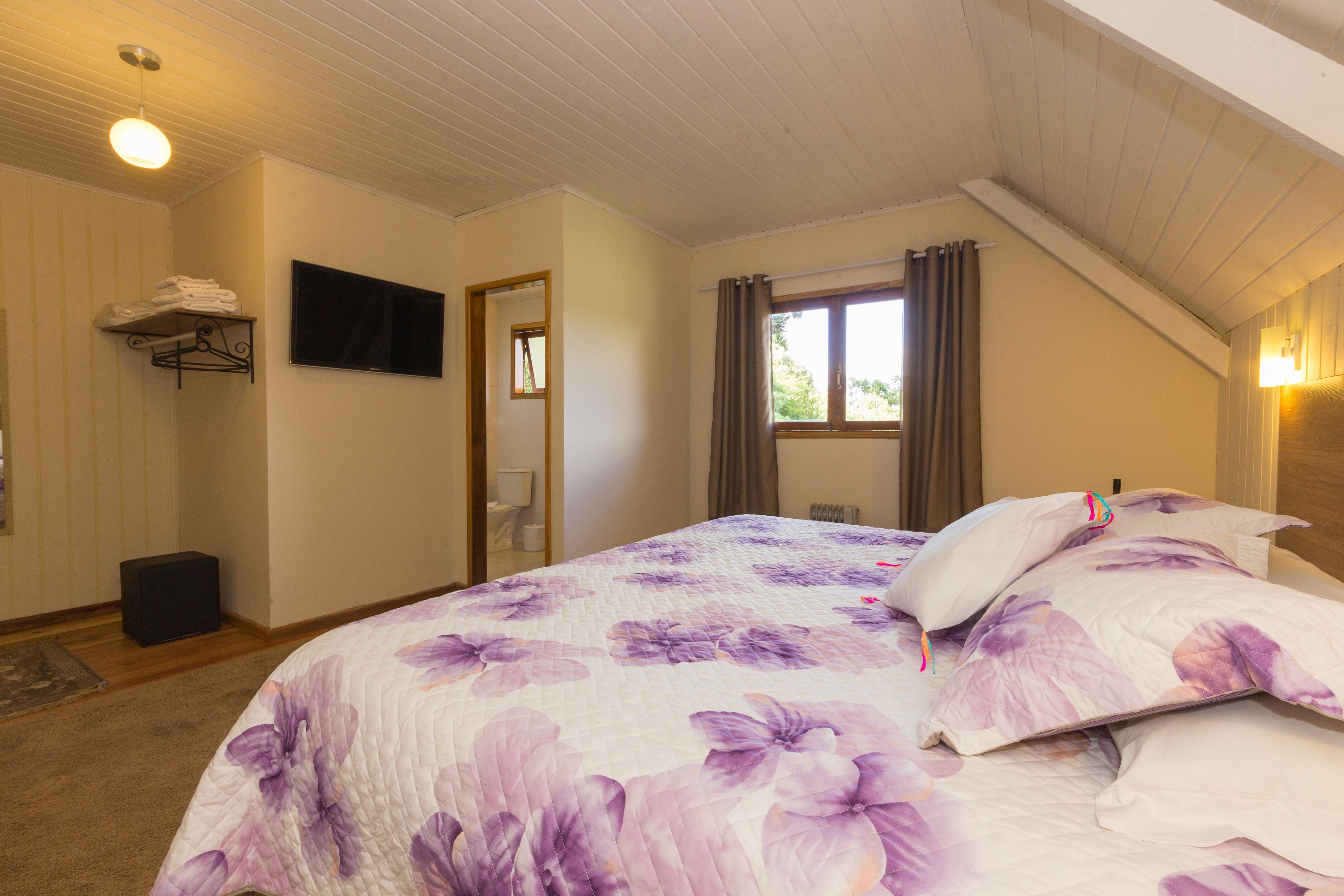 A bedroom with a bed, a television, a window with curtains, and a radiator.