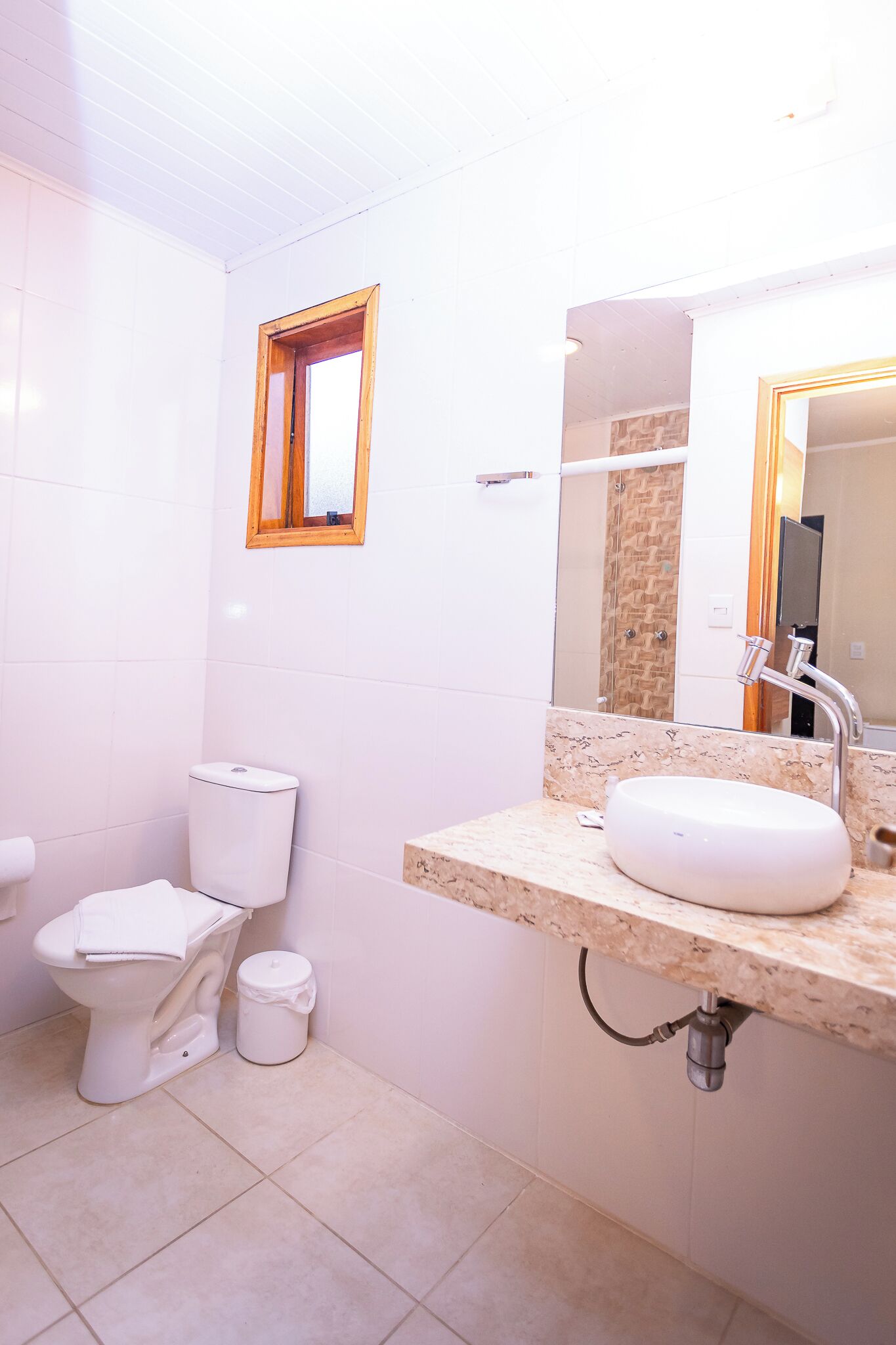 A bathroom with a toilet, sink, mirror, and a small window.