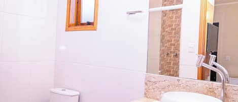 A bathroom with a toilet, sink, mirror, and a small window.