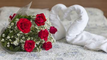 A bouquet of red roses and a white heart-shaped pillow on a bed with a floral-patterned bedspread.